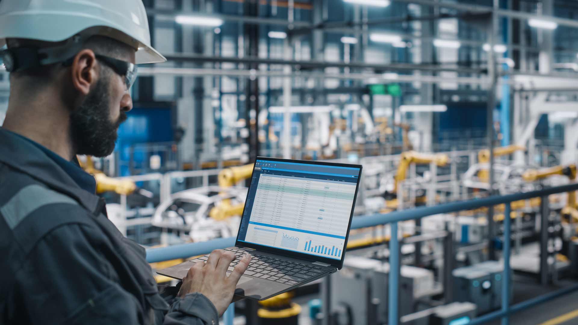 man-looking-at-laptpp-in-factory-wearing-hardhat